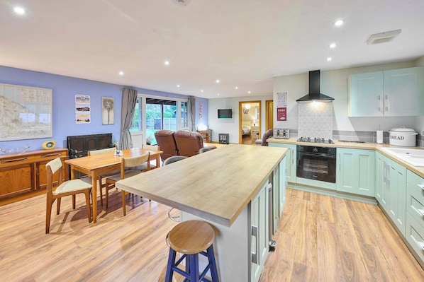 Enjoy meals in this kitchen and dining area, featuring an oven, range hood, and wooden table.