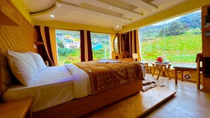 A spacious bedroom with a large bed, a wooden floor, and a view of a lush landscape through large windows. - Rozana Retreat (Ootacamund)