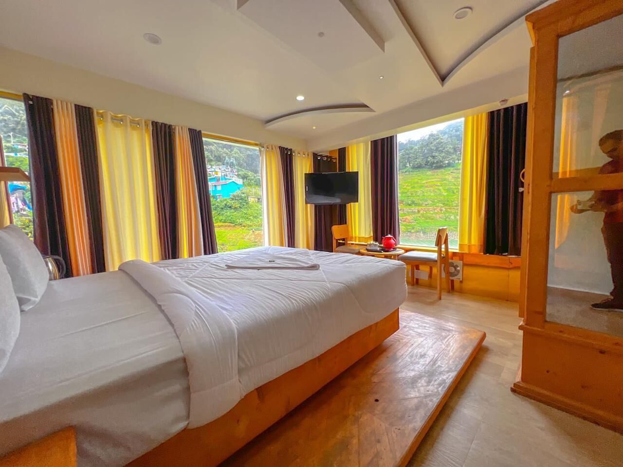 Hotelkamer met een groot bed, een televisie, een houten kast en uitzicht op groen.