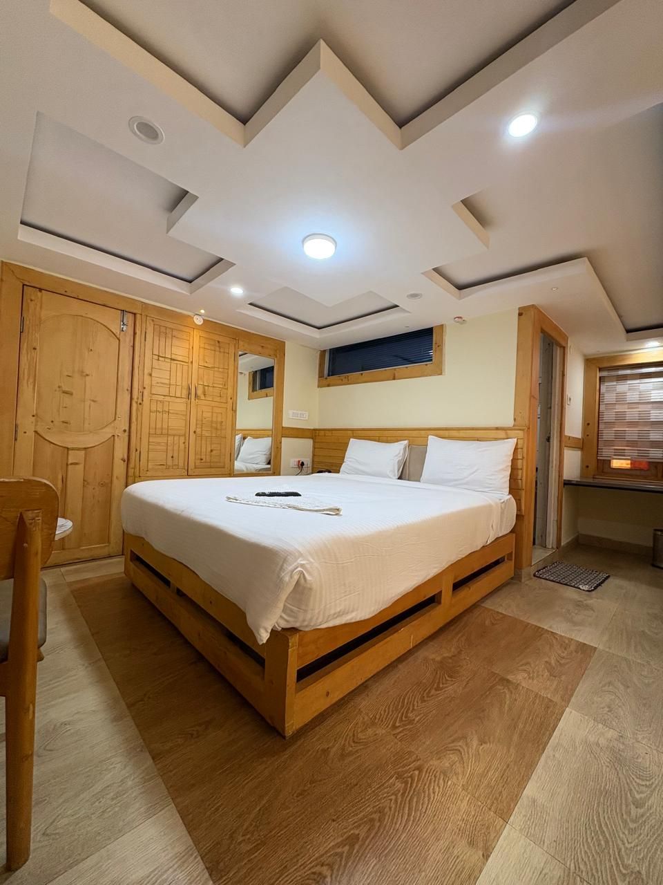 A bedroom with a large bed, wooden wardrobe, and a desk with a chair.