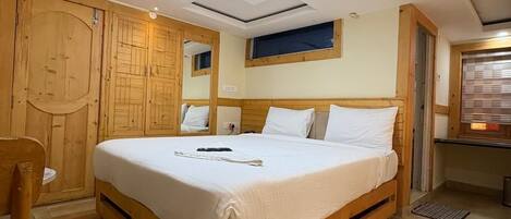 A bedroom with a large bed, wooden wardrobe, and a desk with a chair.