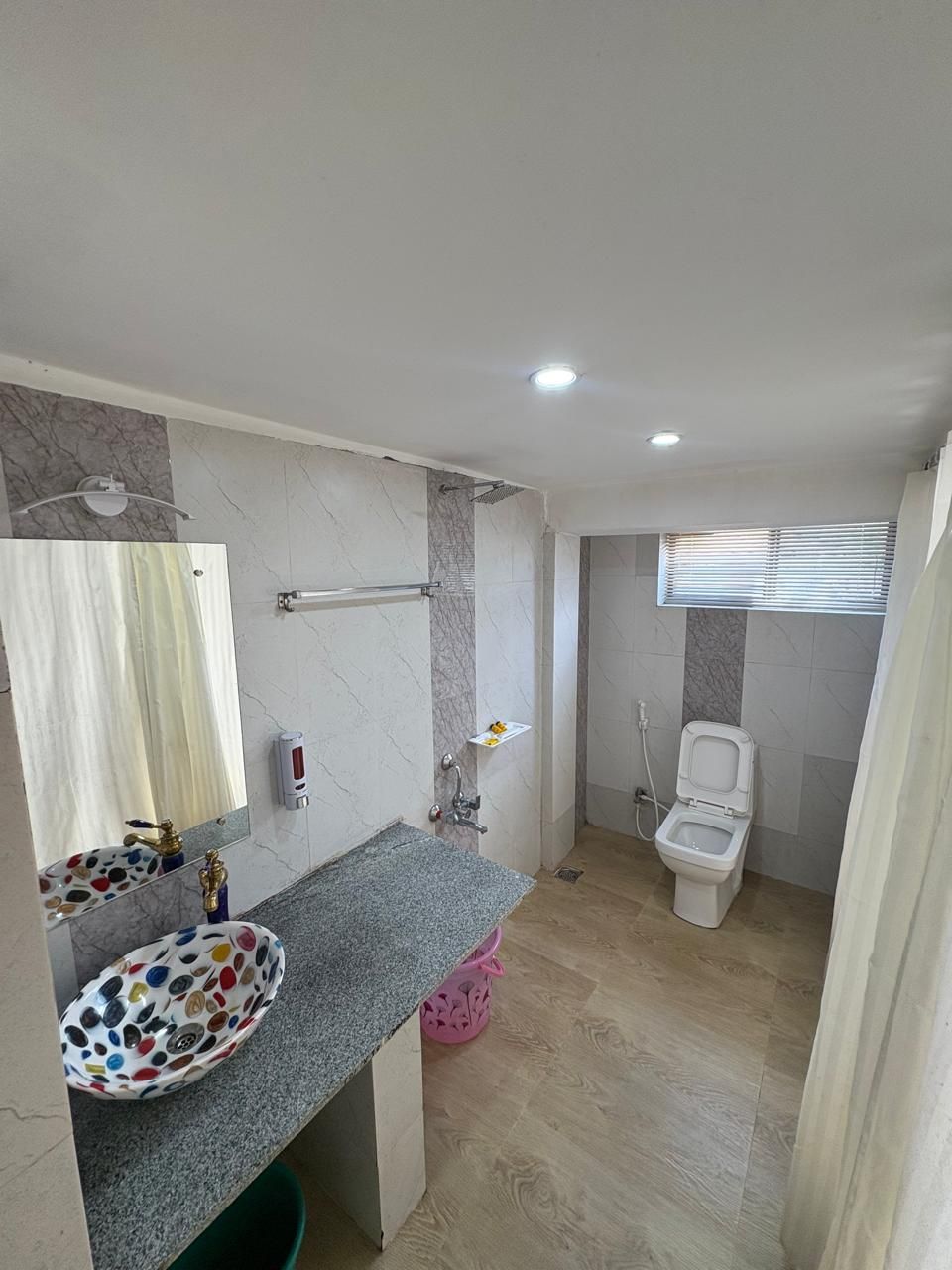 Un baño con pared de mármol, un lavabo con un recipiente de colores, un inodoro y una zona de ducha.