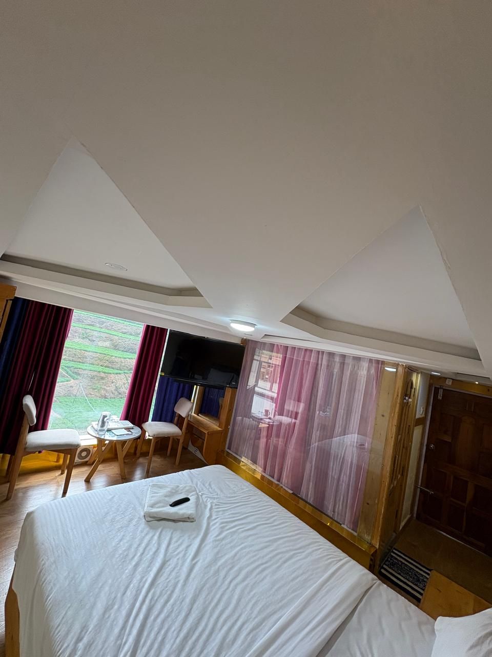 A hotel room with a bed, a desk, a chair, and a window with curtains.