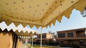 A covered outdoor area with a patterned ceiling, a stone pathway, and a building with balconies in the background. - Imperia Resort by The Sky Imperial (Nathdwara)