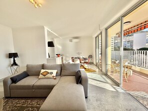 A modern living room with a grey sofa, a small side table, and a large window offering a view of the city. - 2-room apartment with terrace near beaches and parking in Ajaccio (Ajaccio)