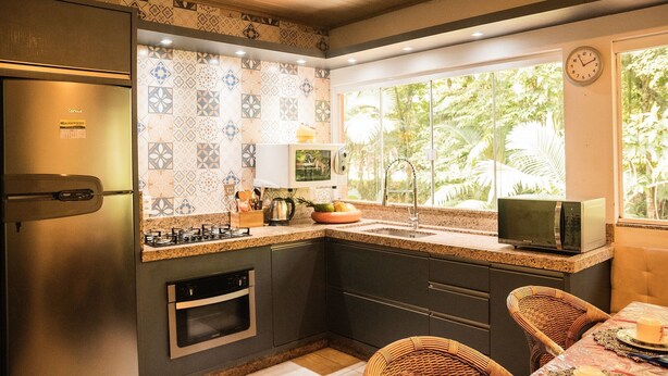 Cozinha equipada com frigorífico, fogão, micro-ondas e lava-loiça. Uma janela oferece vista para o verde lá fora.