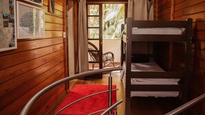 Interior de uma cabana de madeira com uma beliche, um tapete vermelho e quadros nas paredes.