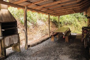 Un espacio al aire libre rústico con una mesa y bancos de madera, una parrilla y una bicicleta.