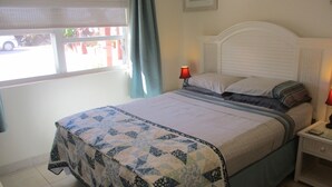 Una cama bien tendida con colcha, dos lámparas de noche y una ventana con cortinas.