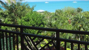 Vista de una playa tropical con dos veleros en el agua, vegetación exuberante y un cielo azul despejado.
