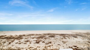 Una playa con cielo despejado, dunas de arena y una valla en primer plano.