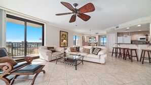 A spacious living room with a large window, a ceiling fan, and a view of the city. - Beachfront 3BR!!  Next door to the Flora-Bama!! (Orange Beach)
