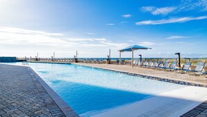 A swimming pool with lounge chairs and umbrellas, a brick walkway, and a view of the sea. - Beachfront 3BR!!  Next door to the Flora-Bama!! (Orange Beach)