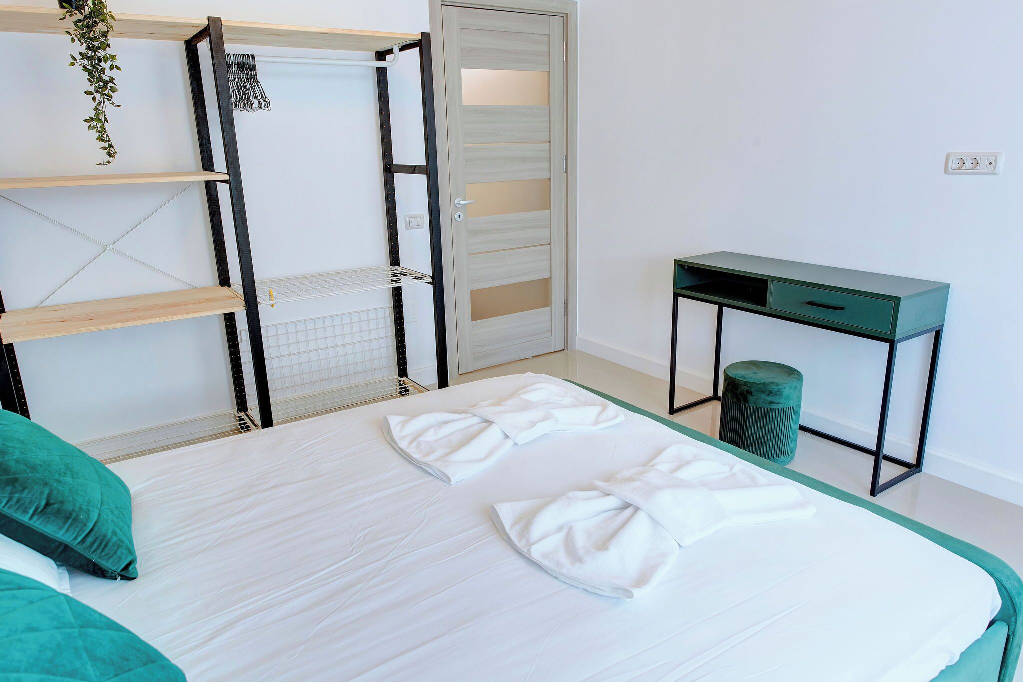 A neatly made bed with white bedding, a green cushion, and a desk with a drawer.
