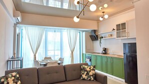 A modern living room with a sofa and a dining area, a kitchen with green cabinets and a black refrigerator, and a ceiling light fixture. - Cnc Zev Apartment (Navodari)