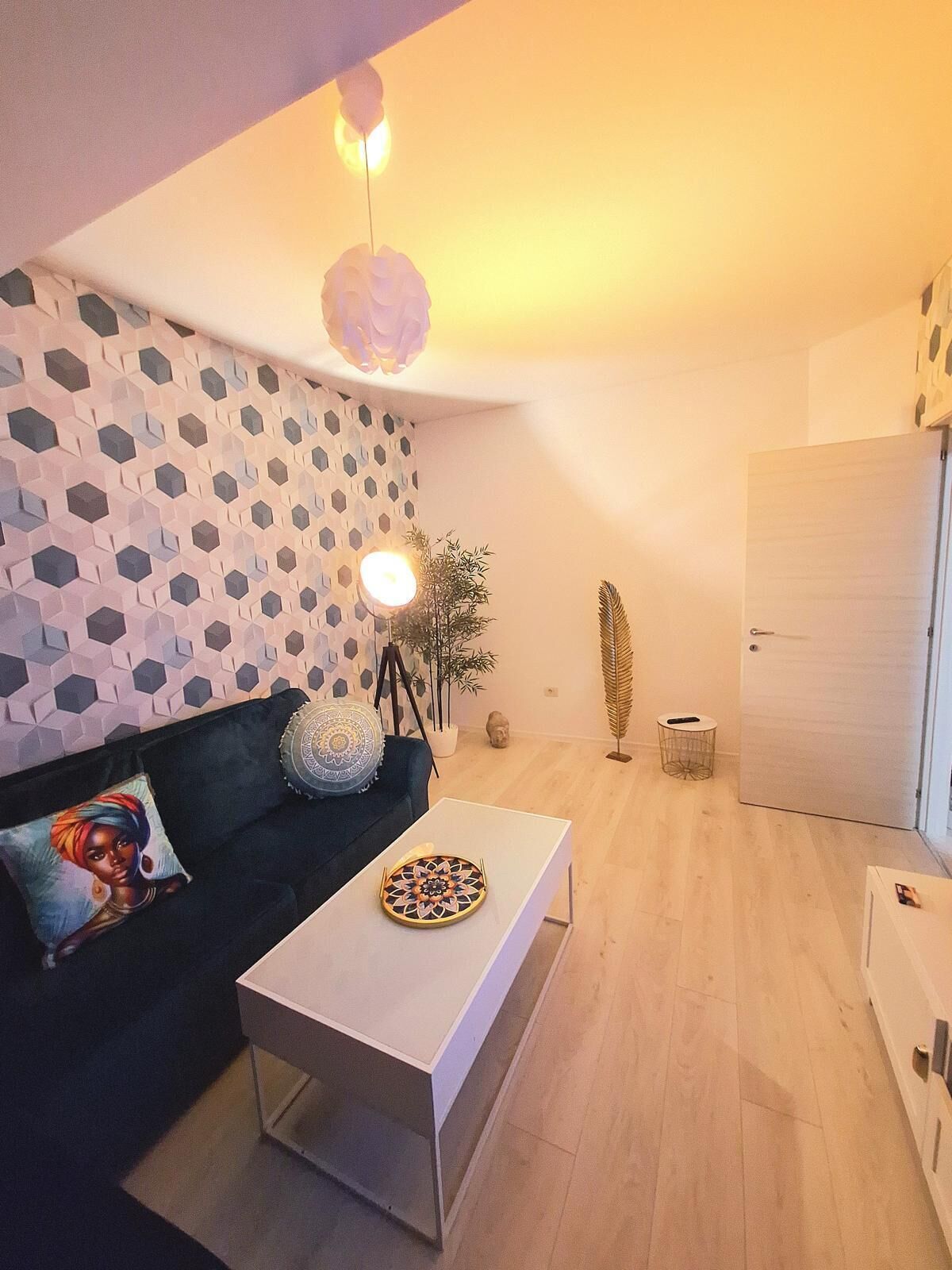 Una sala de estar moderna con un sofá oscuro, una mesa de centro blanca y una pared con estampado geométrico.