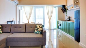 A modern living room with a sofa and a dining table, a kitchen with green cabinets, and a large window with curtains. - Cnc Zev Apartment (Navodari)