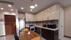 A modern kitchen with a wooden dining table, two chairs, and a built-in oven. - King David standard two bedroom 24 (Tbilisi)