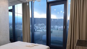 A bedroom with a large bed, a view of a cityscape through floor-to-ceiling windows, and a chandelier. - King David standard two bedroom 24 (Tbilisi)