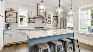 A modern kitchen with a large island, bar stools, pendant lighting, and a view of the outdoors. - Blue Mountain "Drift Away" | 4BR | Pool Access | 2 BIkes (Santa Rosa Beach)