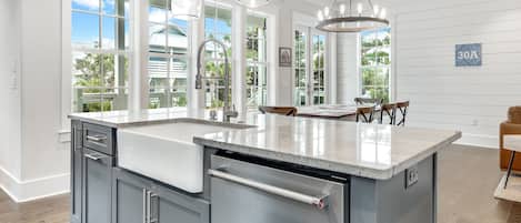 A modern kitchen with a large island, white cabinetry, and a view of the outdoors.