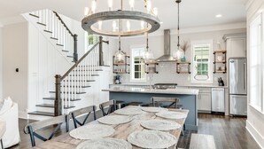 A modern kitchen with a central island, stainless steel appliances, and a staircase with a wooden railing. - Blue Mountain "Drift Away" | 4BR | Pool Access | 2 BIkes (Santa Rosa Beach)