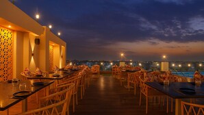 A restaurant with outdoor seating overlooking a body of water, featuring wooden tables and chairs, and warm ambient lighting. - Royal Prime - A City Center Botique Hotal in Jaipur (Jaipur)
