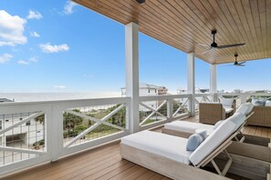 A wooden deck with white railings, lounge chairs, and ceiling fans overlooking a beach. - Dog-Friendly Gulf View Home with Pool (Port St Joe)