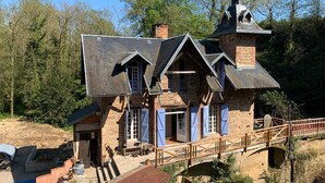 Ein rustikales Steinhaus mit steilem Dach, einer Holzbrücke und einem kleinen Turm.