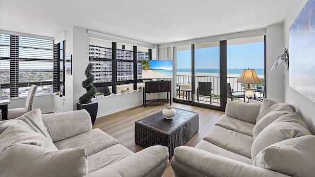 A spacious living room with a large window offering a view of the beach and ocean. - Two-Balcony Beachfront Condo | Pool/Tennis/Grills (Marco Island)