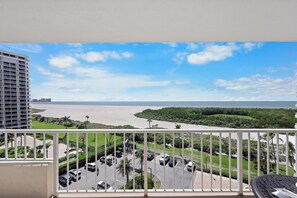 A balcony with a view of a beach, parking area, and greenery.