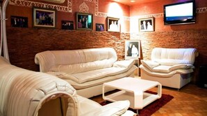 A living room with two white leather sofas, a white coffee table, and a flat-screen TV mounted on the wall. - Résidence Des 4 Chemins (Beni Mellal)