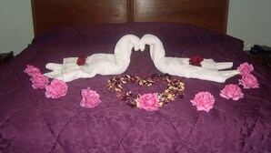 A bed with a purple bedspread, two swan-shaped towels, pink flowers, and a garland of dried flowers. - Résidence Des 4 Chemins (Beni Mellal)