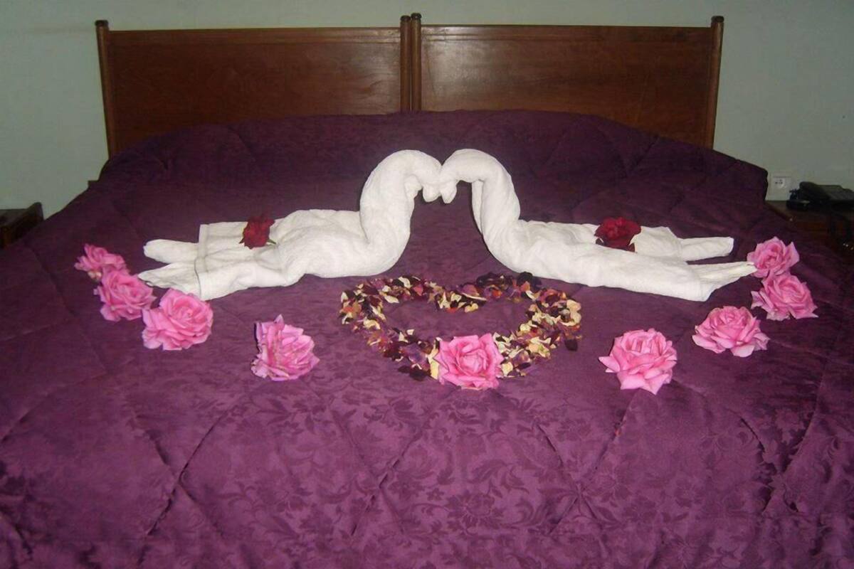 Ein Bett mit einer violetten Tagesdecke, zwei schwanenförmigen Handtüchern, rosa Blumen und einer Girlande aus getrockneten Blumen.