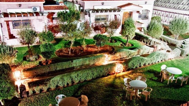 A courtyard with a central water feature, surrounded by neatly trimmed hedges and trees. There are outdoor seating areas with tables and chairs. - Résidence Des 4 Chemins (Beni Mellal)