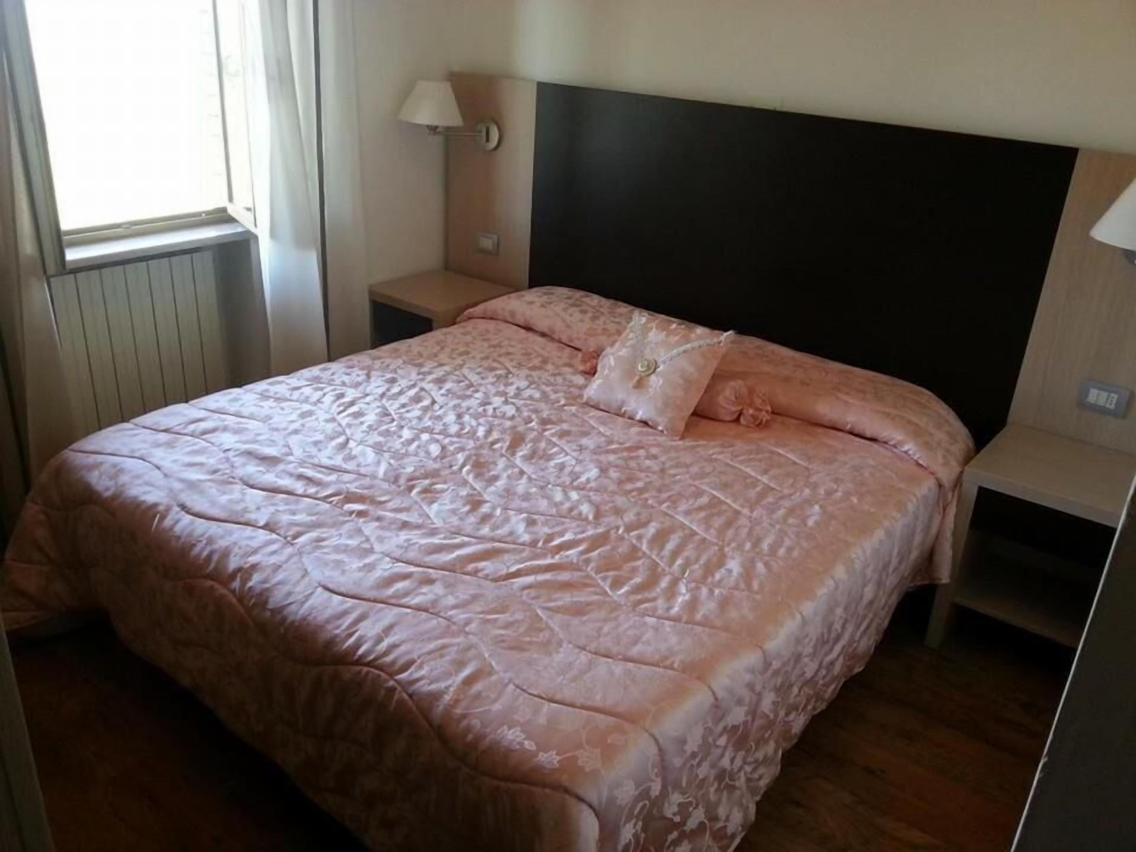 Un dormitorio con cama, mesita de noche, lámpara y ventana.