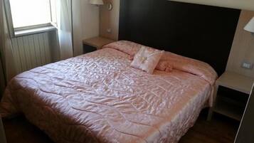 Un dormitorio con cama, mesita de noche, lámpara y ventana.