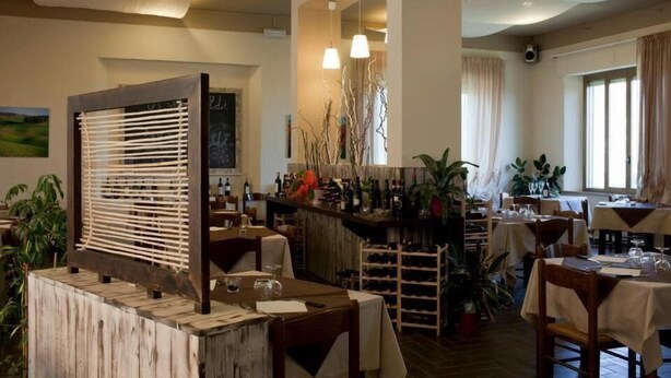 A restaurant with wooden tables, chairs, and a bar area with wine bottles. - Hotel Garibaldi (San Quirico d'Orcia)