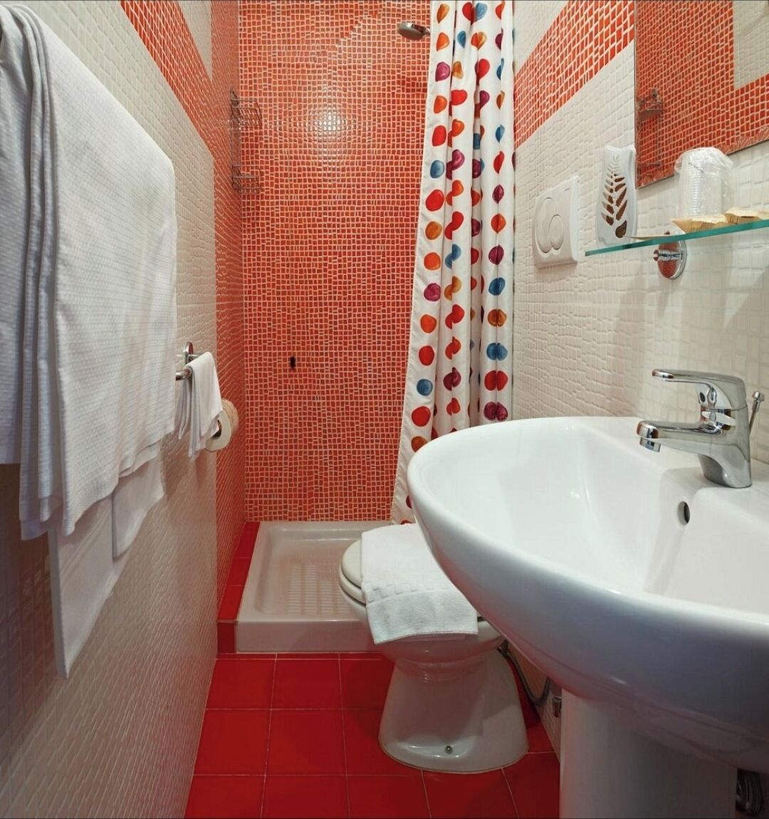 Un baño con un lavamanos blanco, una ducha con mosaicos rojos y un inodoro blanco.