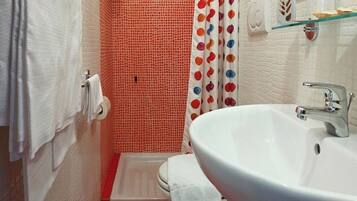 A bathroom with a white sink, a shower with red mosaic tiles, and a white toilet.