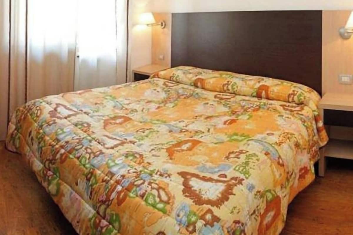 Ein Hotelzimmer mit einem großen Bett, einem Kopfteil, zwei Nachttischen und einem Fenster mit Vorhängen.