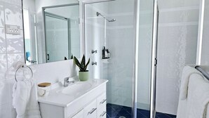 A modern bathroom with a white vanity, a glass shower enclosure, and a potted plant.