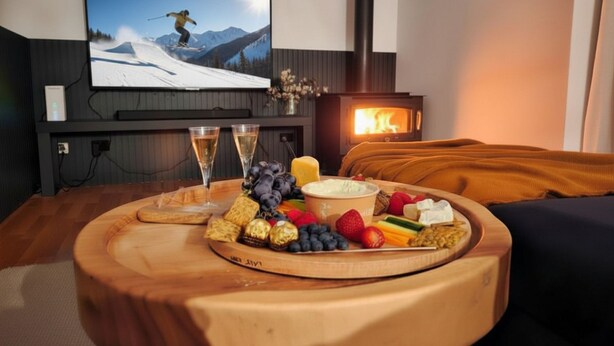 A cozy room with a fireplace, a television displaying a skier, and a wooden table with snacks and drinks.