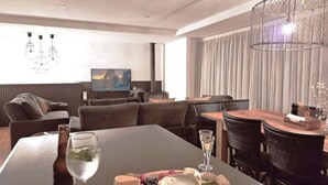 A modern living room with a dining area, featuring a large table, sofas, and a television.