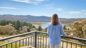 A person standing on a balcony overlooking a scenic landscape with hills and a river.