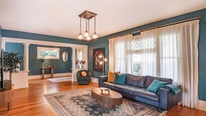 A spacious living room with a dark blue wall, a leather sofa, a coffee table, and a large window with sheer curtains. - B Street Historic House-Min to Convention Cnr, Gaslamp, Balboa-Comp. Bikes (San Diego)