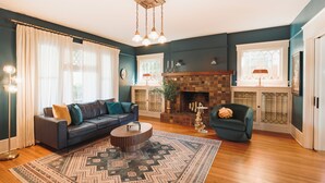 A living room with a dark blue wall, a fireplace, a sofa, a coffee table, and a chair. - B Street Historic House-Min to Convention Cnr, Gaslamp, Balboa-Comp. Bikes (San Diego)