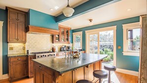 A kitchen with wooden cabinets, a large island with stools, and a view of the outdoors. - B Street Historic House-Min to Convention Cnr, Gaslamp, Balboa-Comp. Bikes (San Diego)