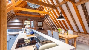 A rustic kitchen with a wooden ceiling, a central island with a stove, and a dining area with a table and chairs. - Belchamp Hall Hayloft and Stables, Belchamp Walter (Belchamp Walter)