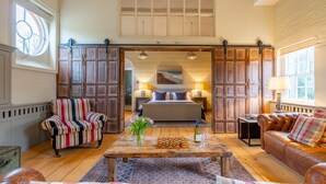 A spacious living room with a large bed, a wooden coffee table, striped armchairs, and a leather sofa. - Belchamp Hall Hayloft and Stables, Belchamp Walter (Belchamp Walter)